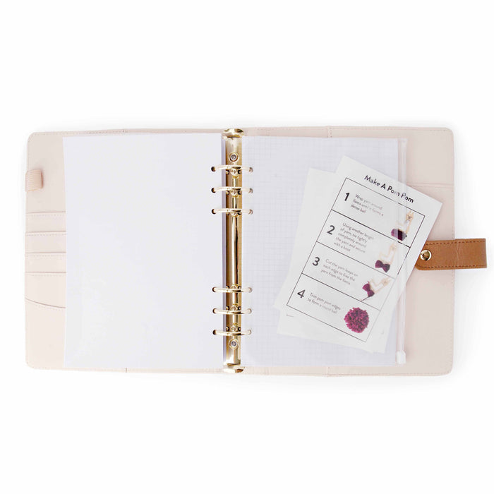 Open pink leather project journal binder with gold rings, graph paper, and zippered pouch with pom-pom instructions