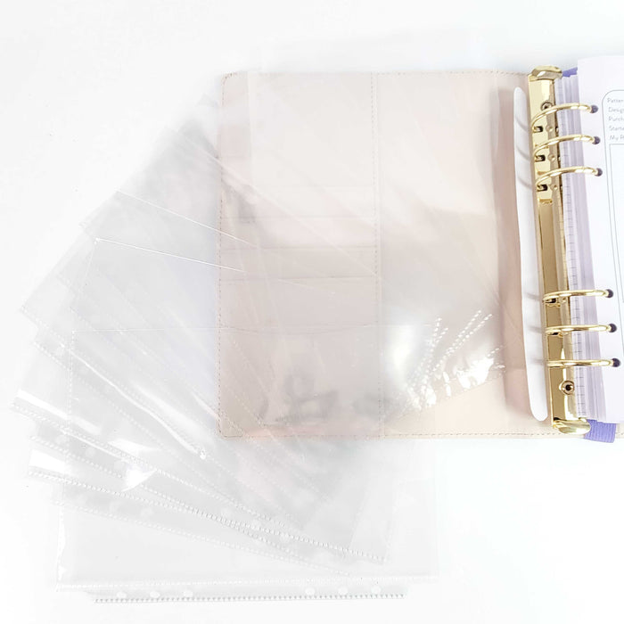 Set of clear page protector sleeves fanned out next to the pink project journal binder with gold rings and project tracking pages