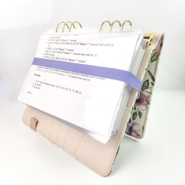 Project journal propped open showing a printed pattern held in place by a lavender elastic band with a floral cover on the back