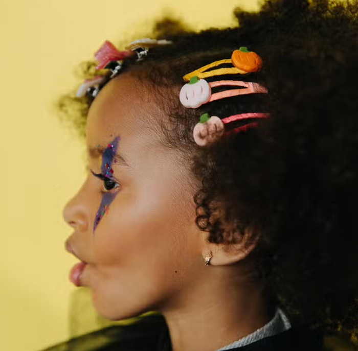 child wearing pumpkin shaped hair clips on yellow background