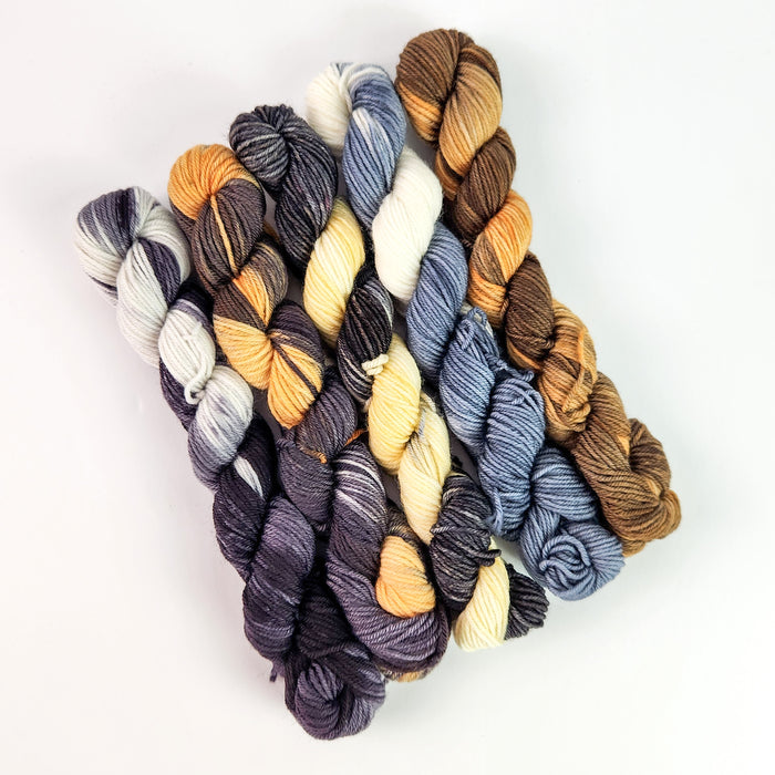 Five mini yarn skeins in dog-inspired colors: gray, charcoal-gold, cream, blue-gray, and brown