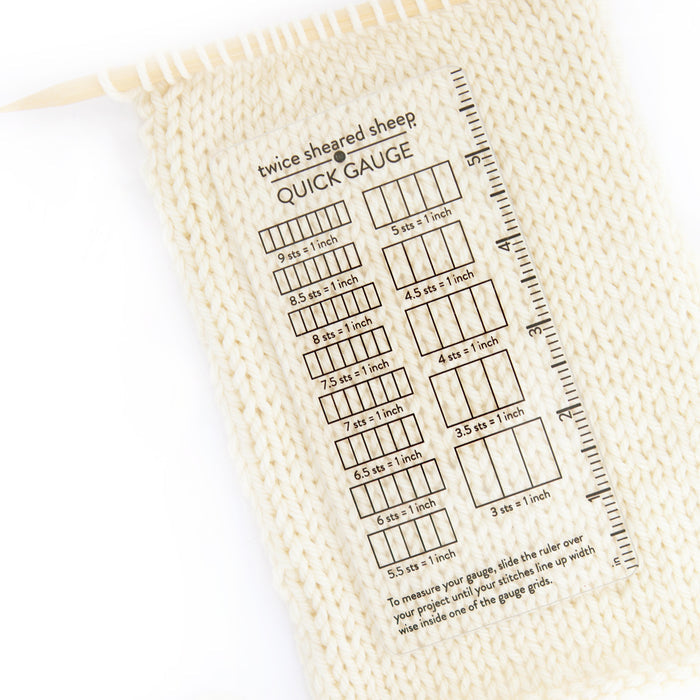 Quick Gauge ruler laid over cream stockinette knitting swatch on bamboo needle showing transparent design