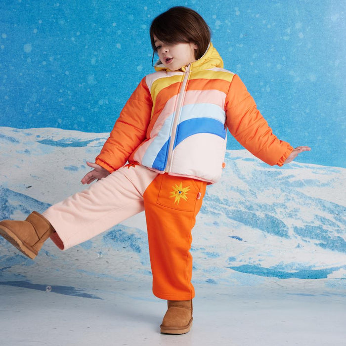 Child wearing a colorful jacket and orange pants against a snowy background