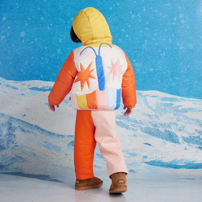 Child wearing a colorful winter outfit with a yellow hood and abstract-patterned vest, standing on snow.