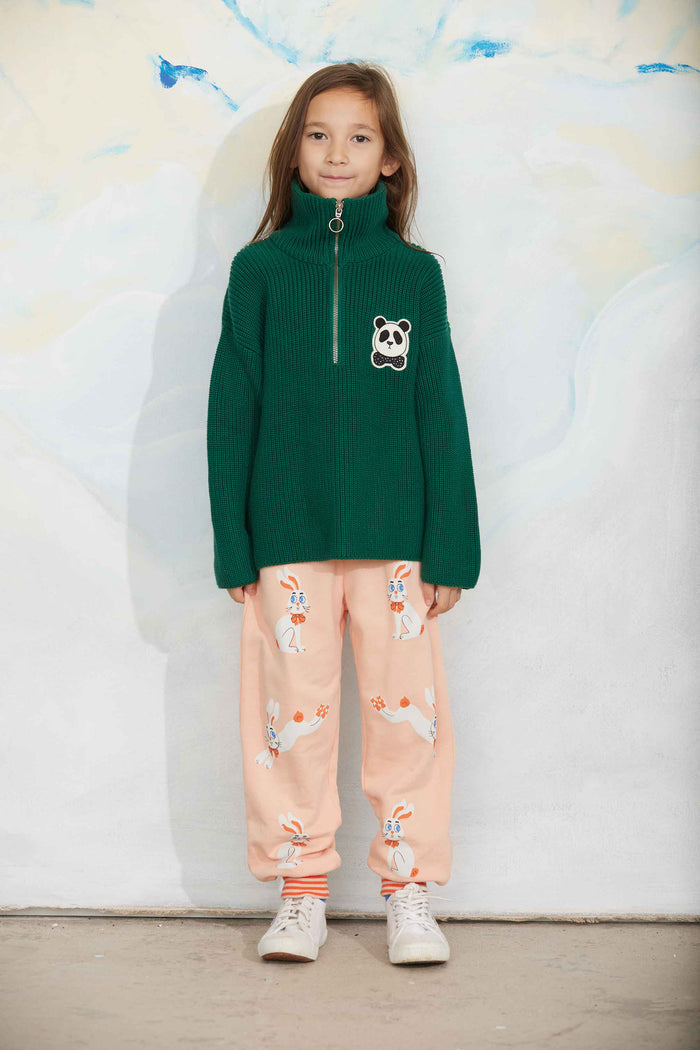 Child wearing a green sweater with a panda design and pink pants with animal prints against a light background