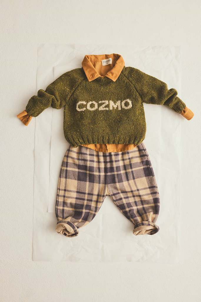 Green sweater with 'cozmo' text and plaid pants on a white background