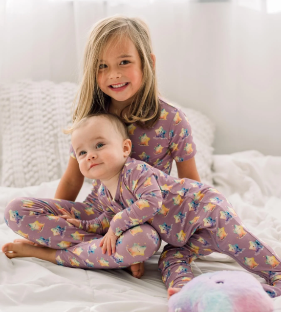 Two children in matching pajamas sitting on a bed.
