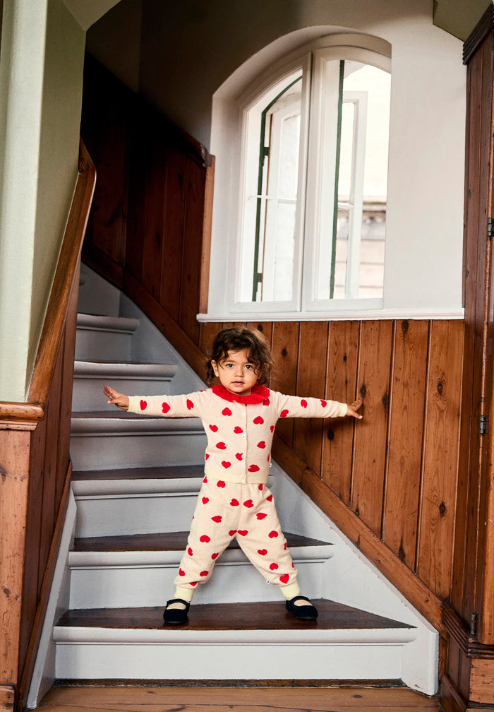 Child in a red and white heart outfit standing on a staircase.