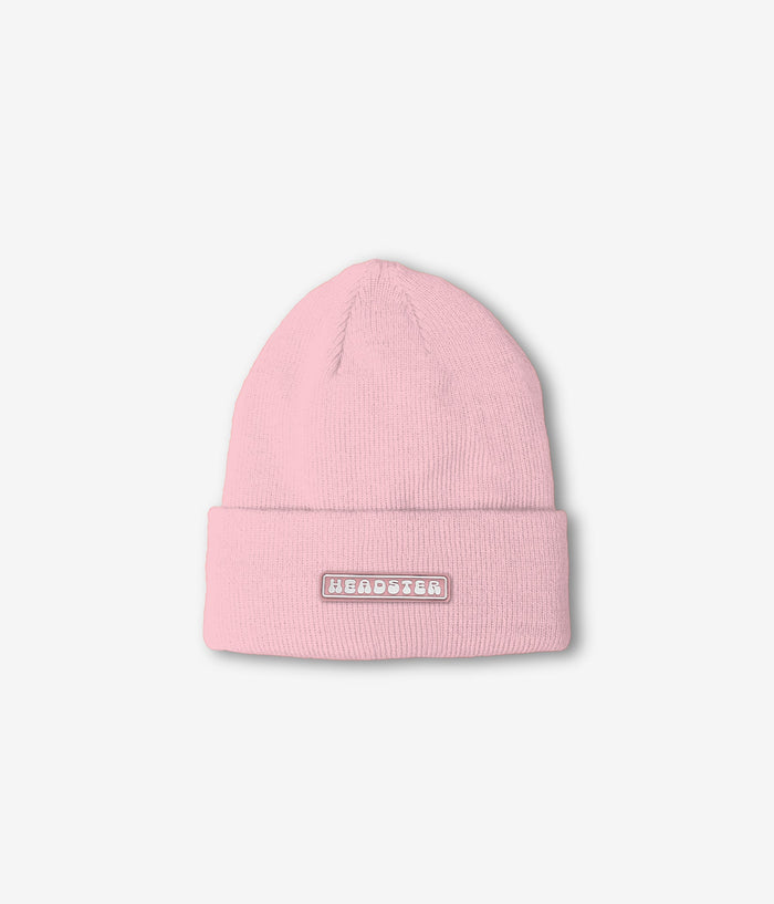 A light pink ribbed knit beanie hat with a folded cuff, featuring a small rectangular metallic patch on the front with the word 'HEADSTER in white lettering.