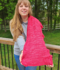 Woman holding the Revenge in Lido Wrap in coral pink lace knit fabric up to show the drape and openwork stitch pattern