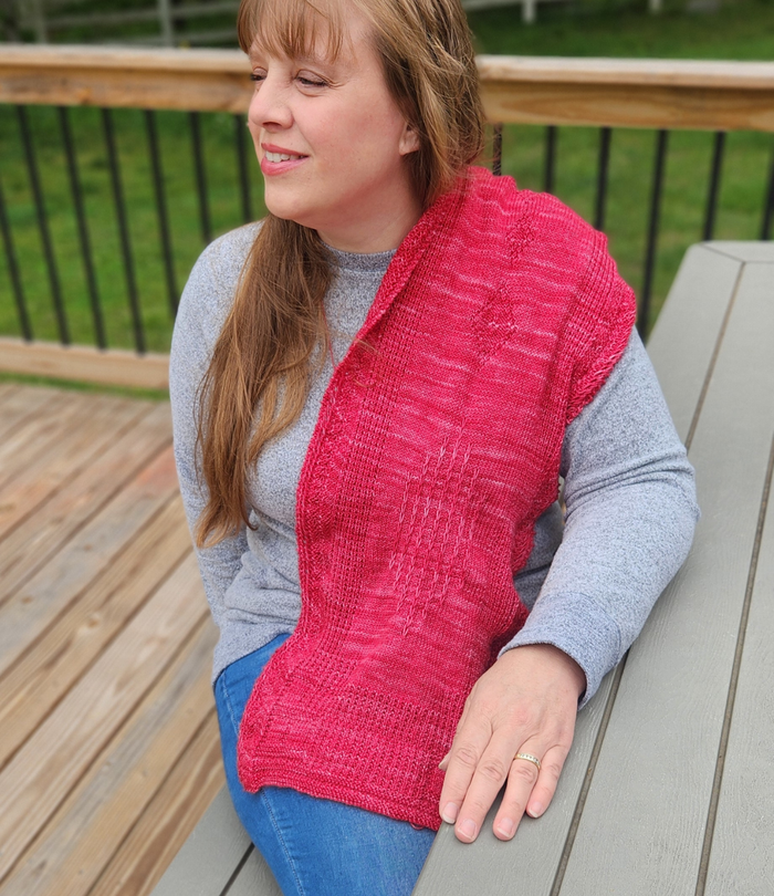 Back view of a woman wearing the Revenge in Lido Wrap in coral pink lace knit draped over her shoulders showing the full width and openwork pattern