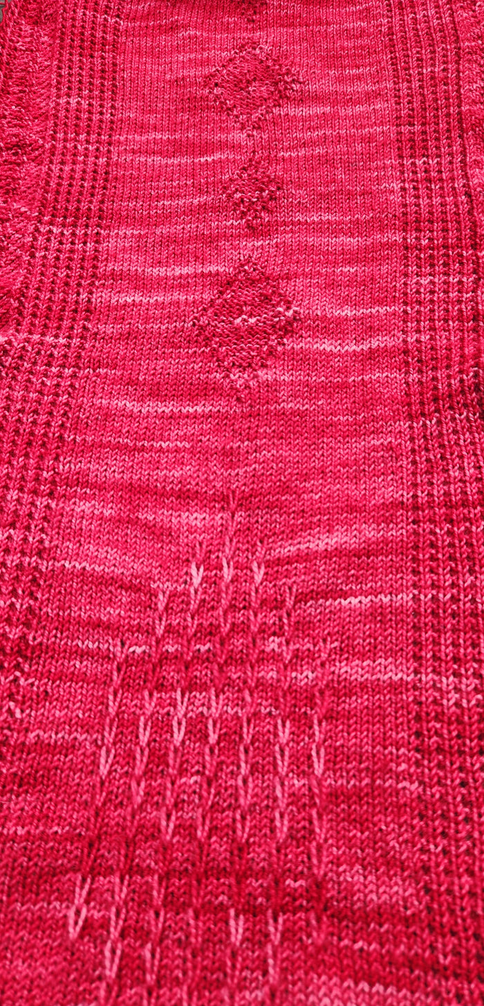 Close-up of the Revenge in Lido Wrap knitted fabric showing the openwork lace stitch pattern in coral pink fingering weight yarn