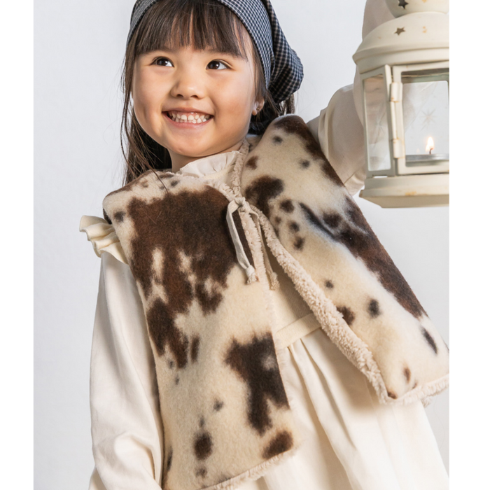 Child wearing a brown and white patterned vest with a lantern in the background