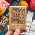 Hand holding the gold Rhinebeck Doodle Card Deck by Pacific Knit Co tuckbox