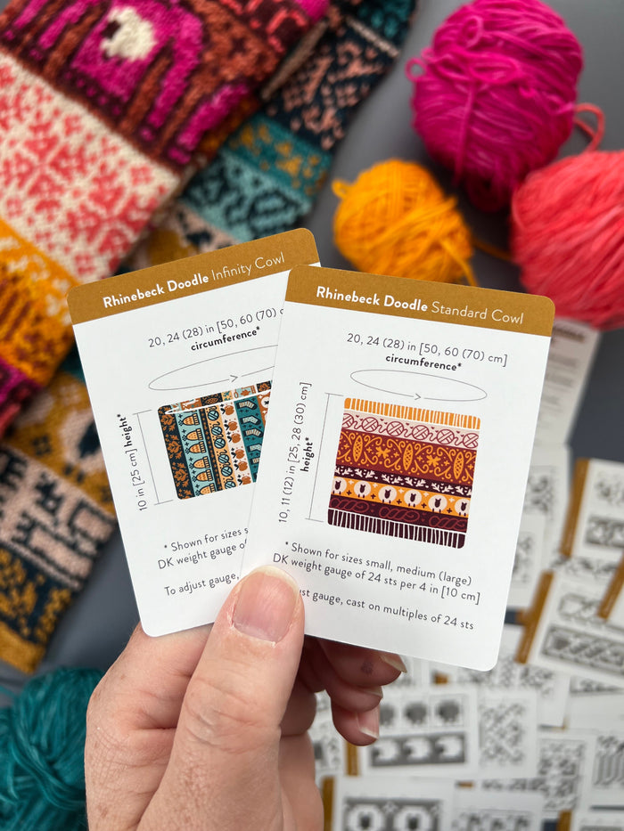 Hand holding the Rhinebeck Doodle Infinity Cowl and Standard Cowl schematic cards
