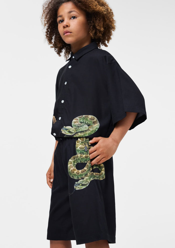 Person wearing a black dress with a large green snake design on a white background
