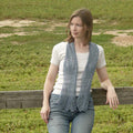 Woman wearing gray-blue Rill lace scarf draped over shoulders with leaf lace pattern visible outdoors by fence