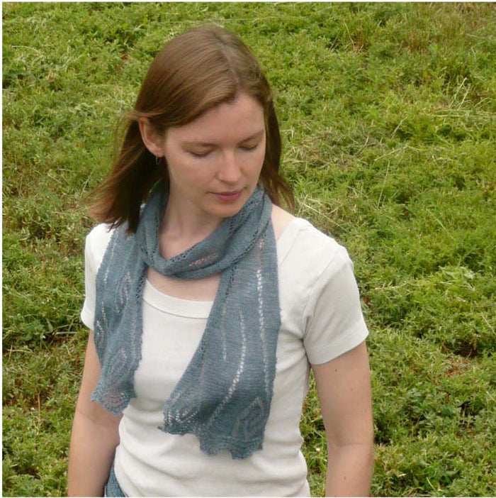 Woman wearing gray-blue Rill lace scarf wrapped around neck outdoors showing delicate leaf lace pattern