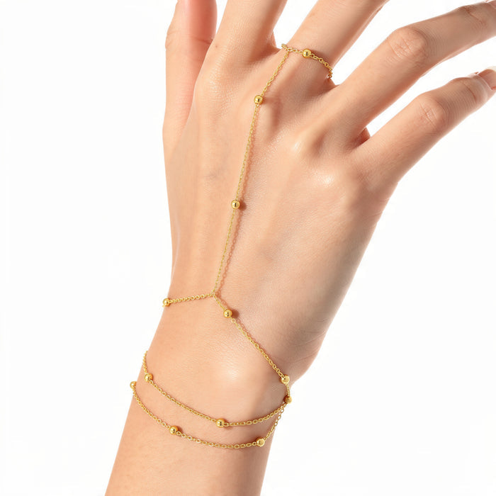 Luxury gold hand chain bracelet worn on manicured hand, double layer bead station chain with Y-shaped connector to finger ring, minimalist gold jewelry on white background