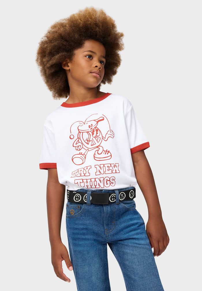 Child wearing a white t-shirt with red accents and blue jeans on a plain background