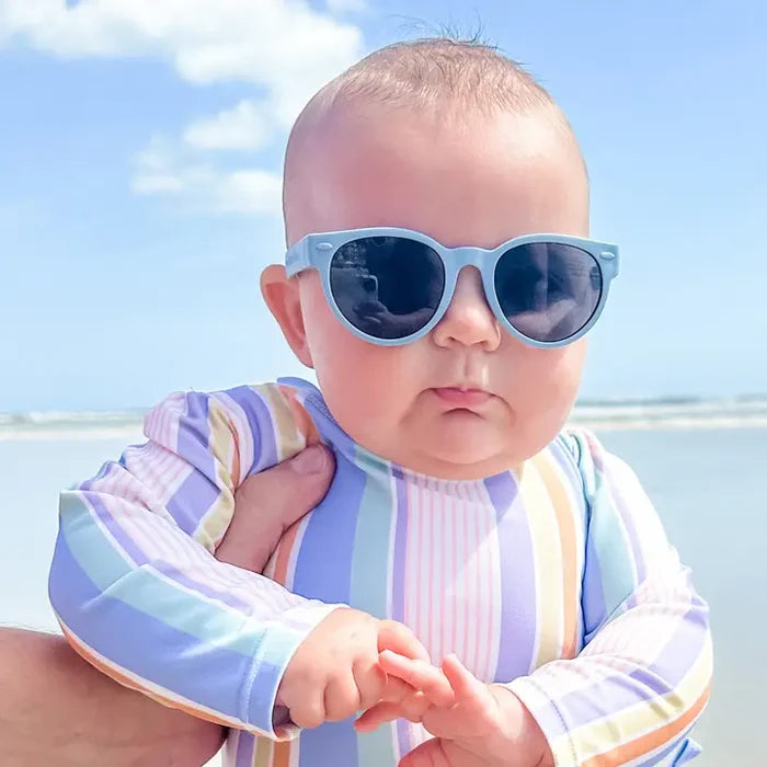 Baby wearing sunglasses and a striped shirt with a beach background