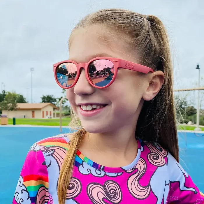 Young girl wearing pink sunglasses with a colorful shirt by a pool