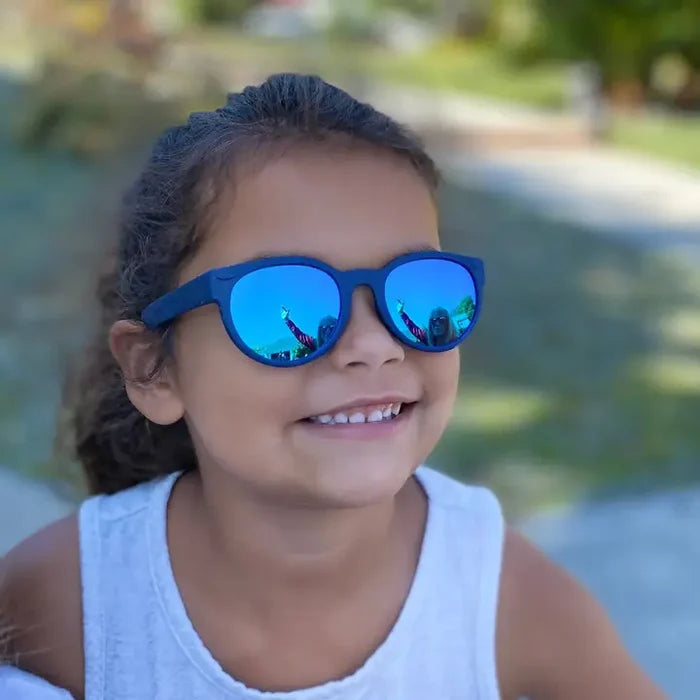 Child wearing blue sunglasses with a blurred outdoor background