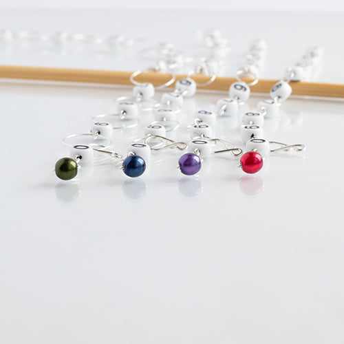 Close-up of four Fairy Lights row counter chains showing numbered beads with green, blue, purple, and red pearl gemstone charms