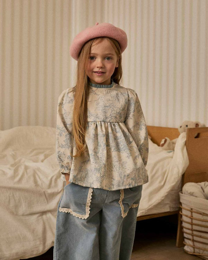 Young girl wearing a floral blouse and pink beret in a cozy room.