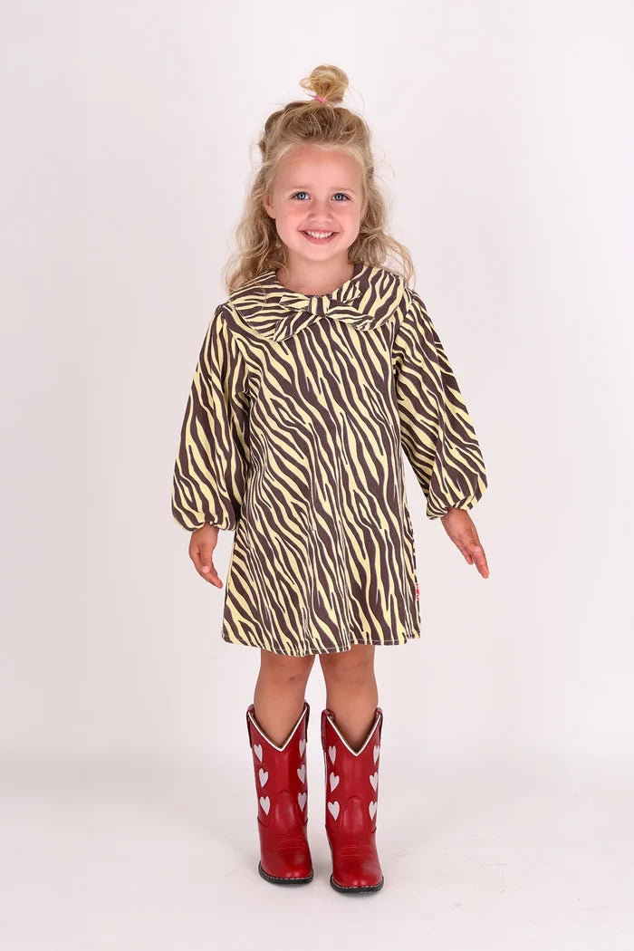 child wearing yellow and brown zebra stripe dress with peter pan collar and bow with red cowboy boots on white background.