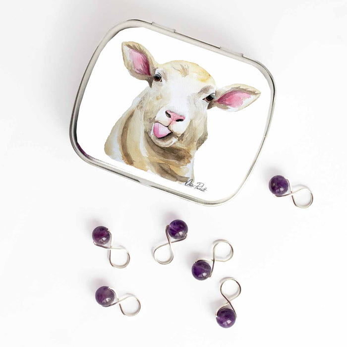 Small hinge-style Sassy Sheep storage tin open beside purple amethyst bead infinity-loop snag-free stitch markers on white background