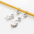 Silver charm stitch markers on a bamboo knitting needle — a giraffe charm and a sheep charm with I and K letter beads on wire rings