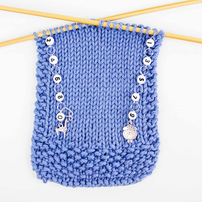 Sheep and llama odd even row counter set in use on blue knitting swatch showing both chains hanging from needles