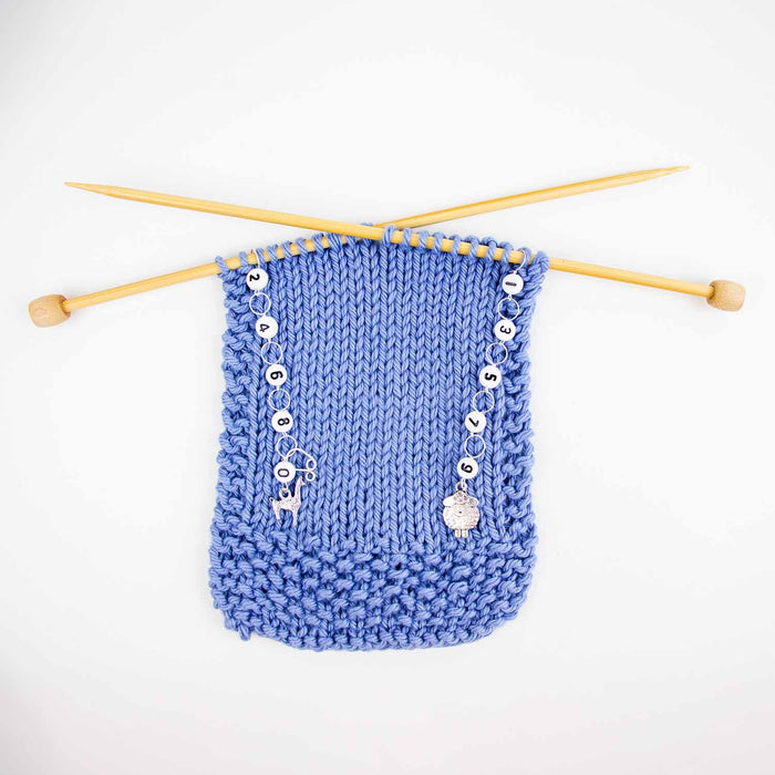 Wider view of sheep and llama row counter set on blue knitting with bamboo needles crossed showing both counters in use