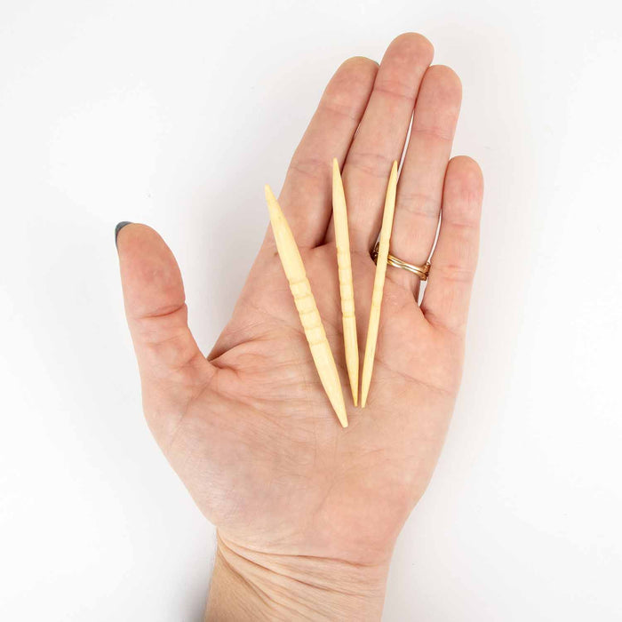 Hand holding three shortie bamboo cable needles in different sizes to show their compact length and double-pointed shape