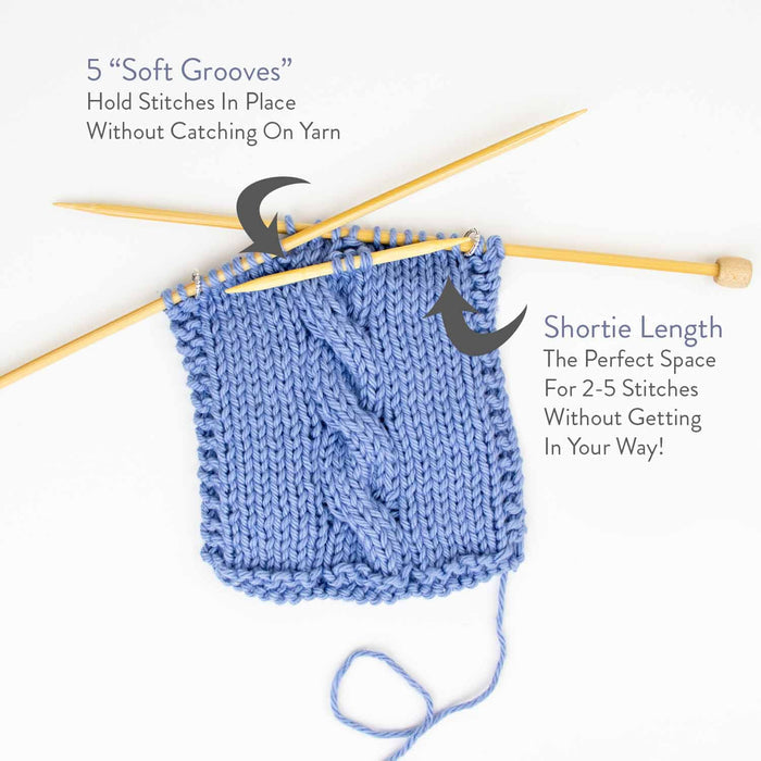 Three shortie bamboo cable needles laid next to a knitting needle and blue yarn to show scale
