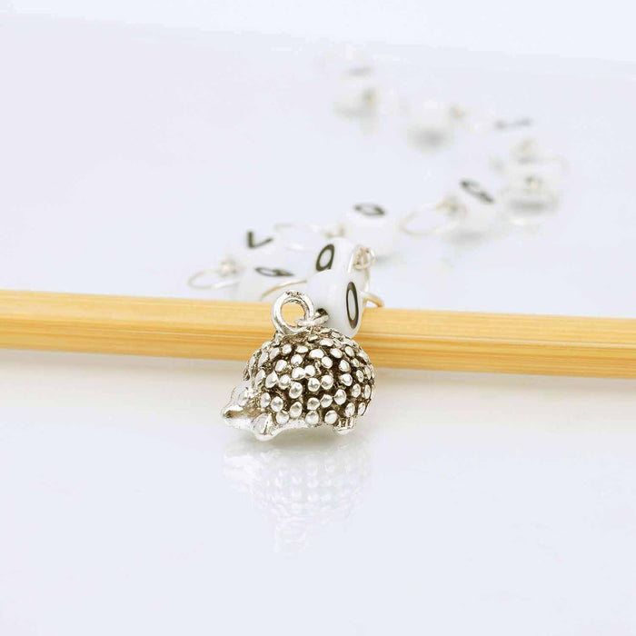 Silver hedgehog charm row counter on a chain with two wooden knitting needles, showing the detailed metallic hedgehog bead