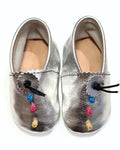A pair of metallic silver leather baby booties with scalloped edges, black drawstrings, and colorful embroidered accents in blue, pink, yellow, and gold on a white background.