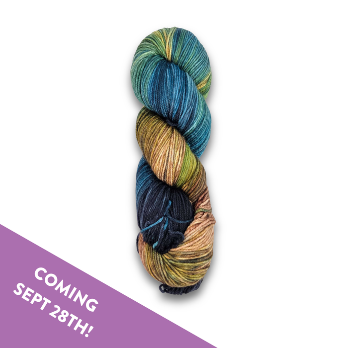 Skein of Yarnaceous Fibers Smuggler's Bay fingering weight sock yarn in deep navy, teal, gold and copper, with a Coming Sept 28th banner