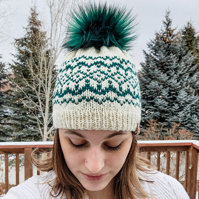 Close-up top view of the Snow Days beanie worn showing the teal and cream Fair Isle snowflake colorwork pattern and teal faux fur pom pom