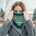 Woman wearing a teal and white stranded colorwork Snow Days Cowl pulled up over her nose outdoors in a snowy winter setting