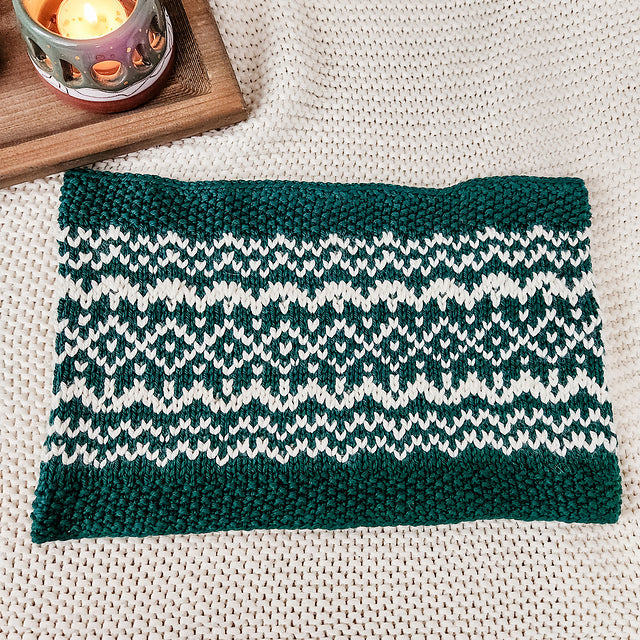 Flat lay of finished Snow Days Cowl showing the teal and cream Fair Isle snowflake and geometric pattern on a cream knit background