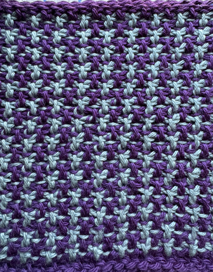 Close-up detail of the Snowfall Tunisian crochet stitch pattern showing the purple and grey two-color colorwork texture