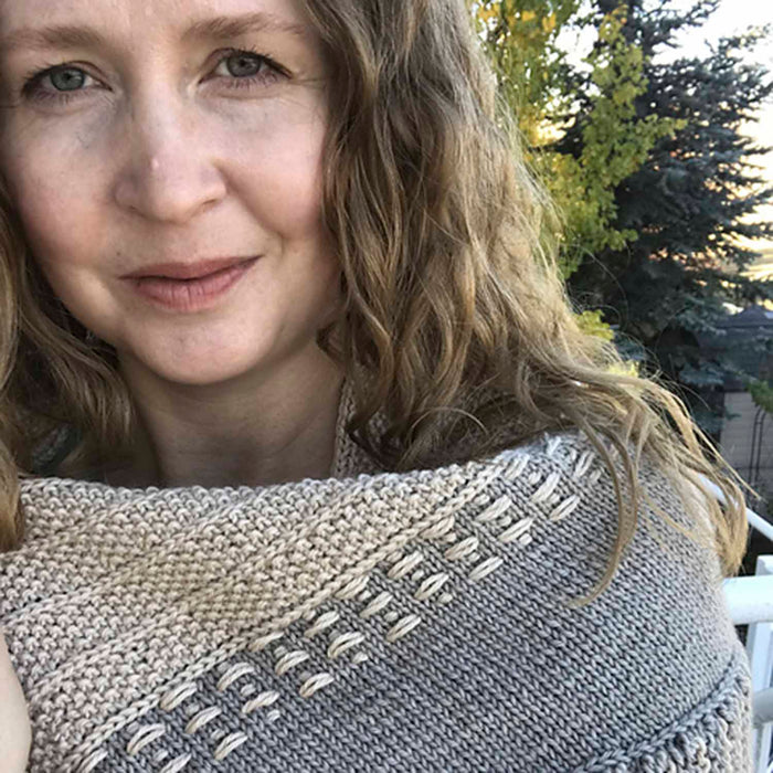 Woman wearing the Snowy Owl shawl in gray and cream with textured stitch detail wrapped snugly around her shoulders outdoors