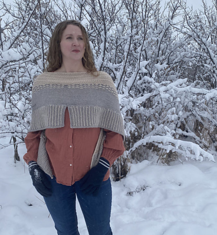 Woman wearing the Snowy Owl shawl draped over her shoulders showing the full width and textured stitch pattern in a snowy setting