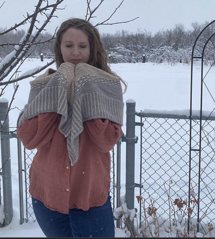 Woman holding the Snowy Owl shawl gathered at her chest showing the drape and textured stitch pattern in gray and cream outdoors in snow