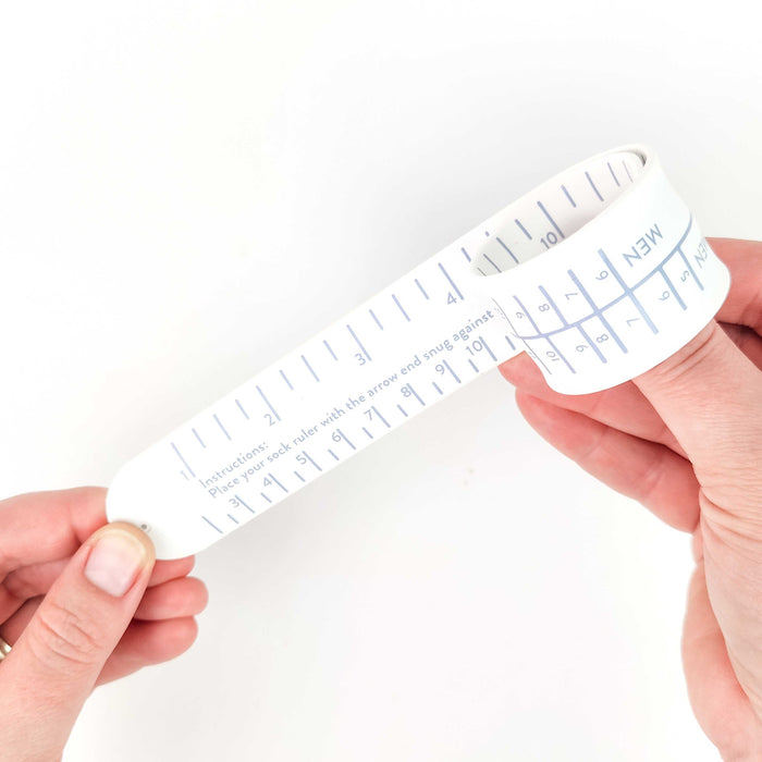 Hands holding a white Sock Sizing Ruler curled into a bracelet shape showing the flexible slap-bracelet design with size markings and instructions printed on the inside