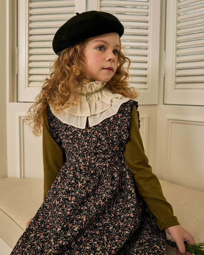 Young girl in a floral dress and black beret sitting on a couch.