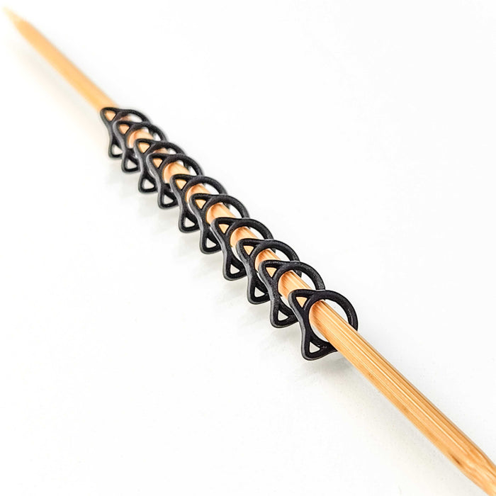 Row of black cat shaped stitch markers lined up on a bamboo knitting needle showing the cat silhouette design with ears