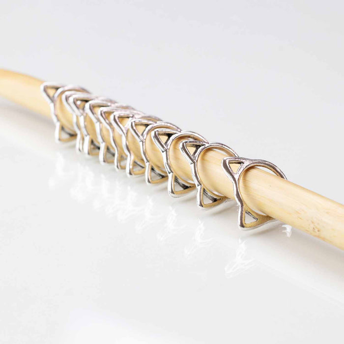 Row of silver cat-shaped stitch markers on bamboo knitting needle showing cat silhouette design
